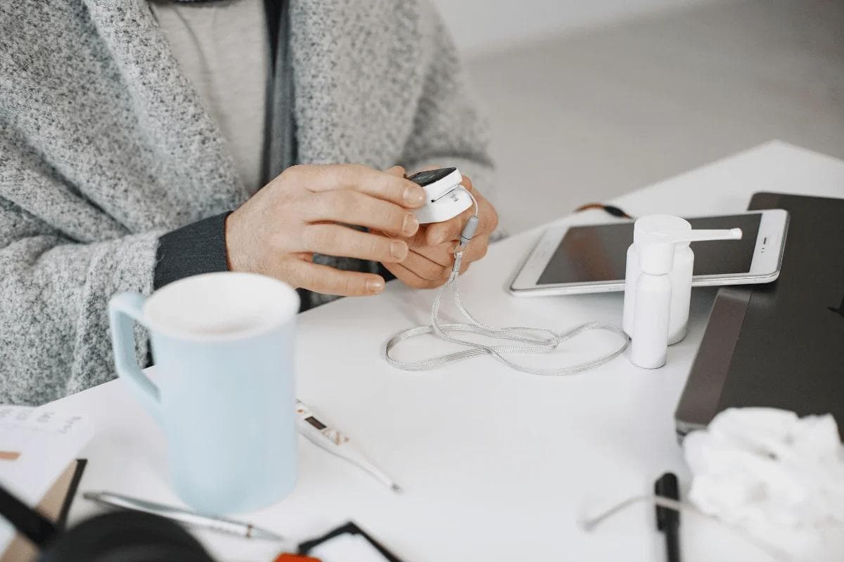 Person using pulse oximeter at home with tablet nearby.