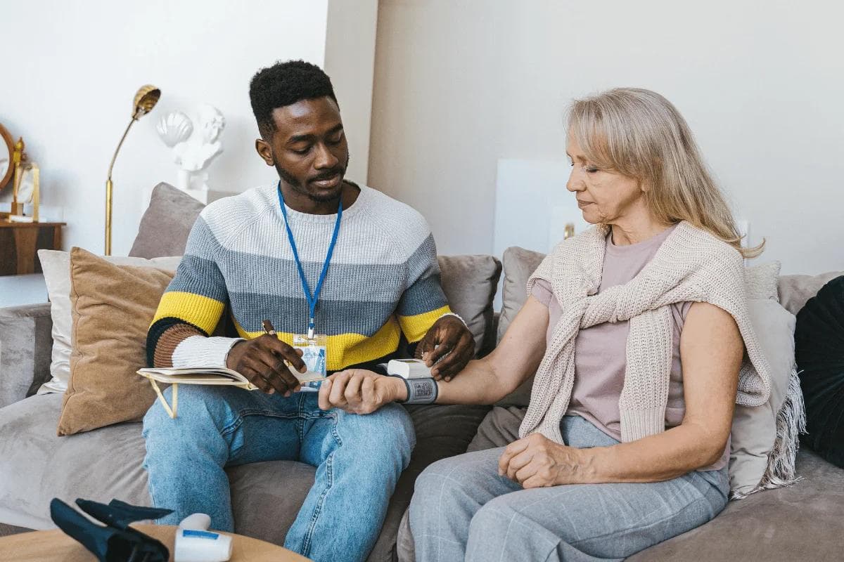 Care worker checking elderly woman’s blood pressure at home.