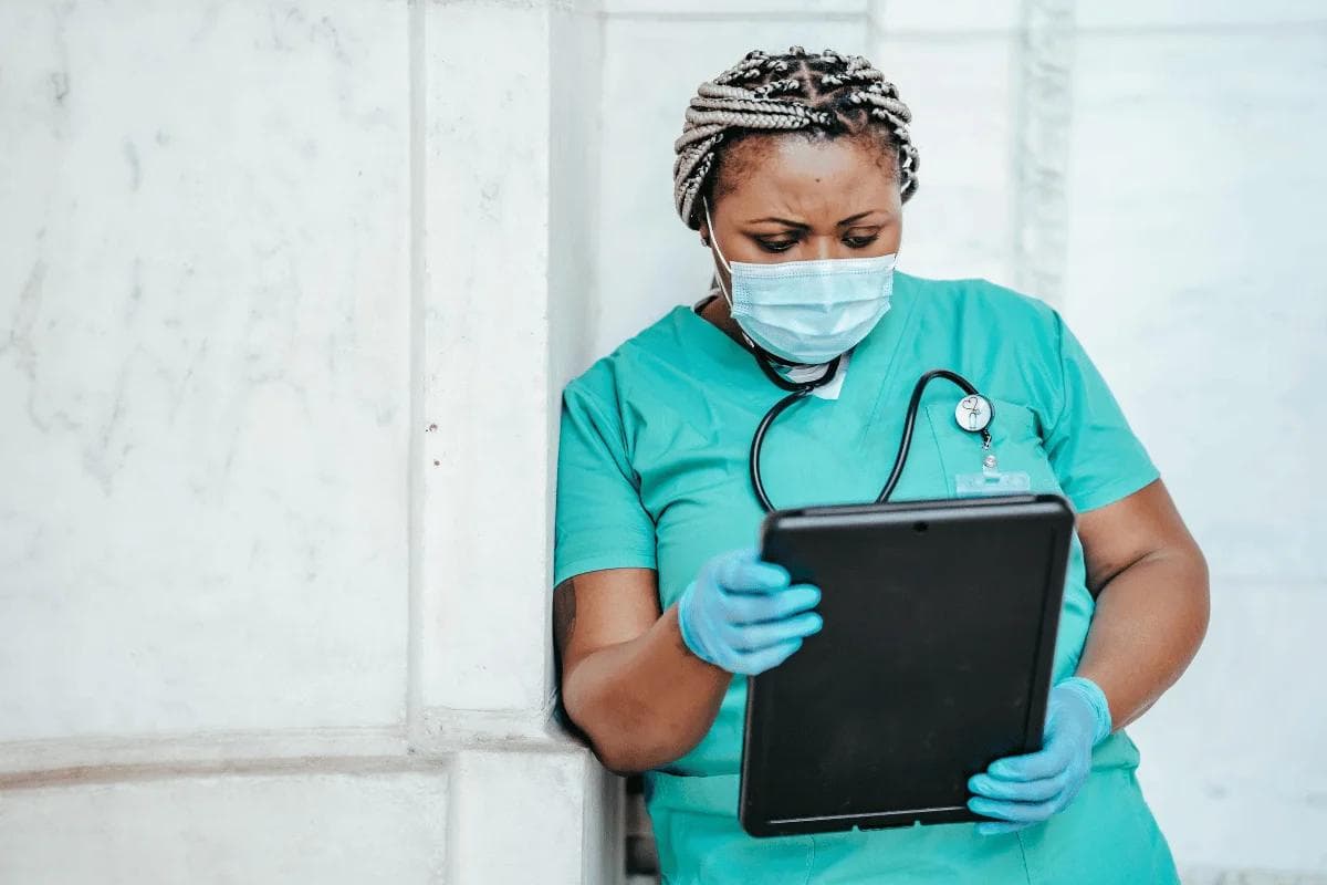Nurse in scrubs reviewing patient data on tablet.
