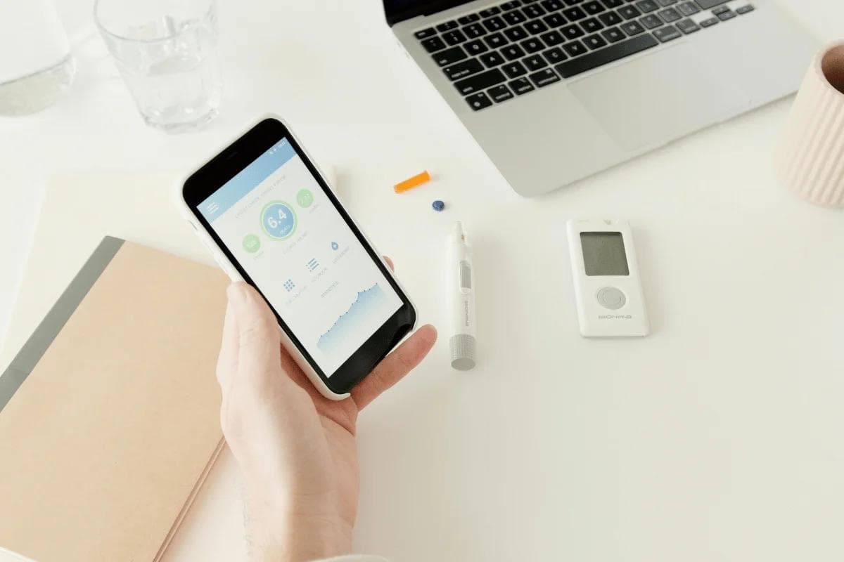 Person checking glucose levels on smartphone app at desk.