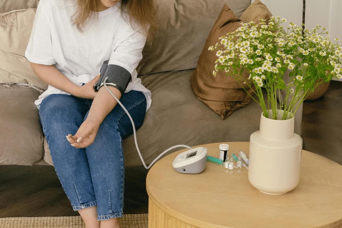 Patient measures blood pressure with electronic cuff in living room.