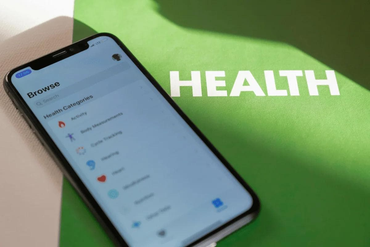Smartphone displaying health app categories on a green surface with large white text "HEALTH" partially in shadow.
