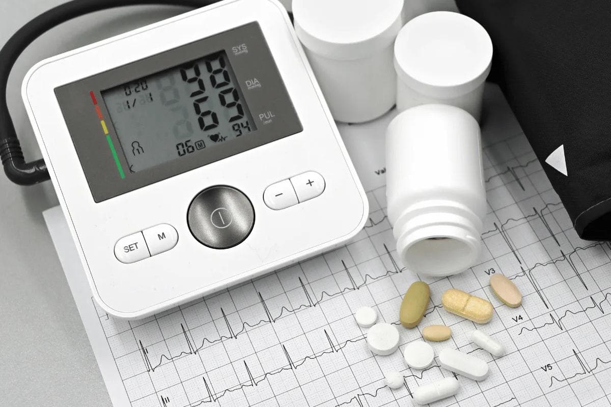 A digital blood pressure monitor displays readings alongside various pills and an ECG printout, highlighting health monitoring.