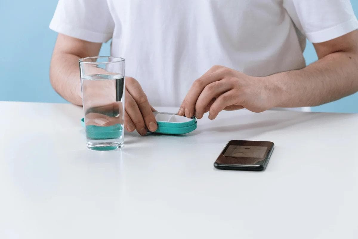 Daily pill routine with water glass and smartphone on table.
